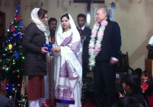 The pastor’s wife giving Dr. Amineh Hoti a Christmas gift while Professor Akbar Ahmed looks on at the Kachi Abadi church in Pakistan.