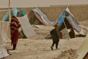 In this undated photo, a woman and a child are seen walking toward a makeshift tent at the Nawabad Farabi-ha camp for internally displaced people in Mazar-e Sharif in northern Afghanistan. Since the recent US pullout from Afghanistan, tens of thousands of refugees have arrived in the United States. Photo credit: UNHCR/Edris Lufti